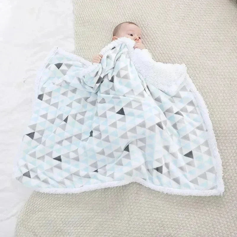 bébé allongé sur un tapis, couvert d'une couverture chaude à motifs triangles bleus et gris