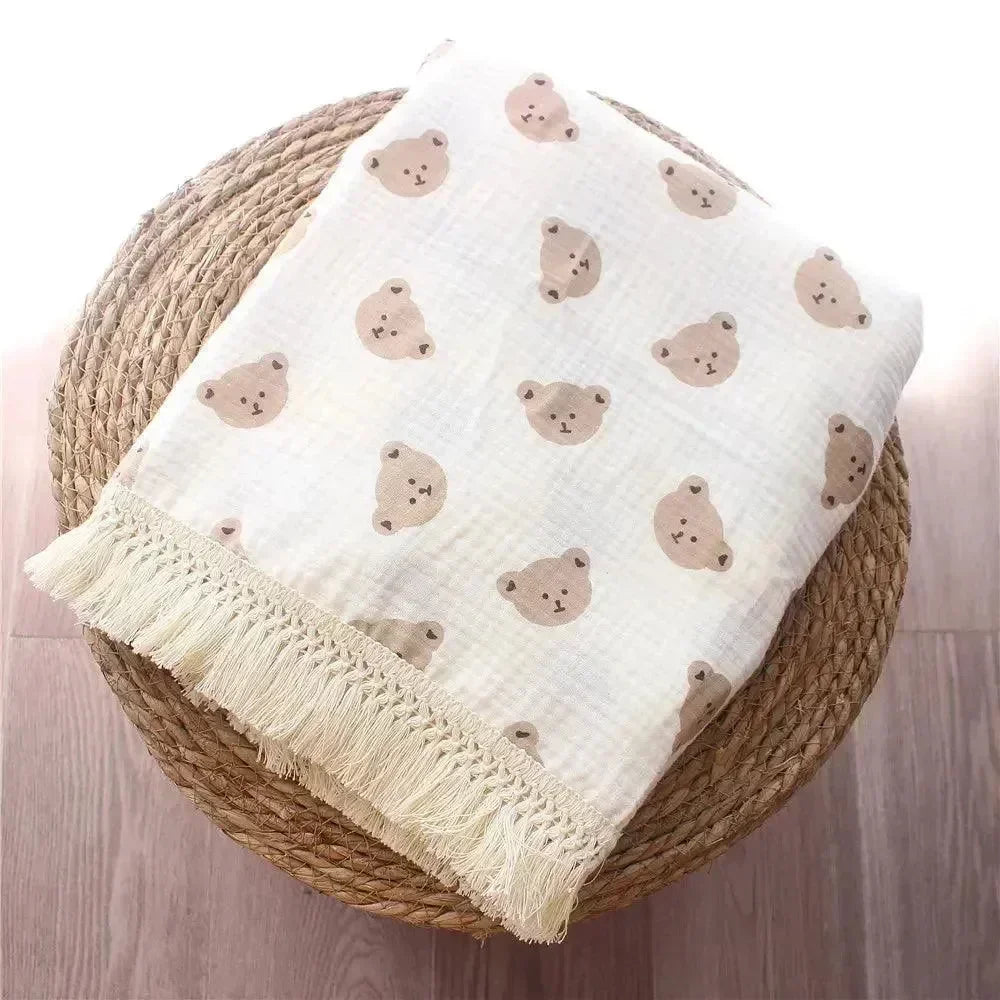 Couverture bébé en mousseline blanche motif têtes d’ours beiges et franges décoratives.