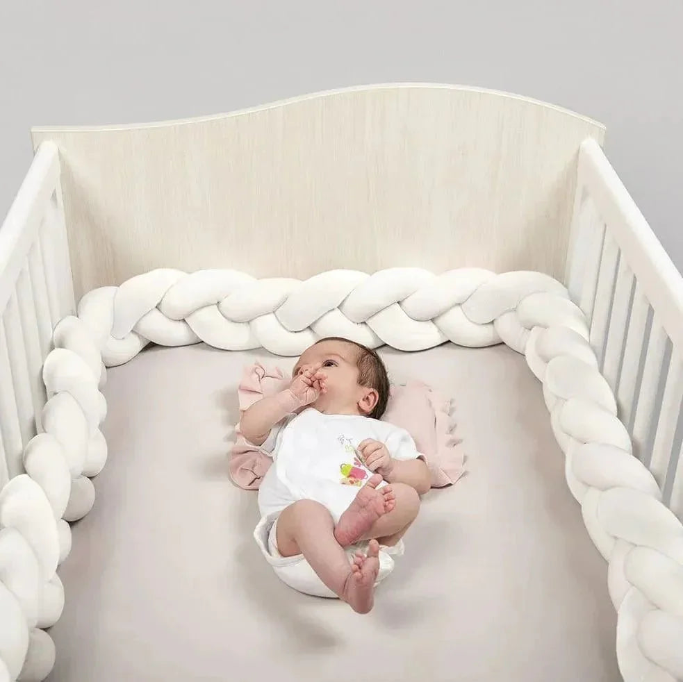 Bébé allongé dans un lit à barreaux avec tour de lit tressé blanc, ambiance douce et sécurisée.