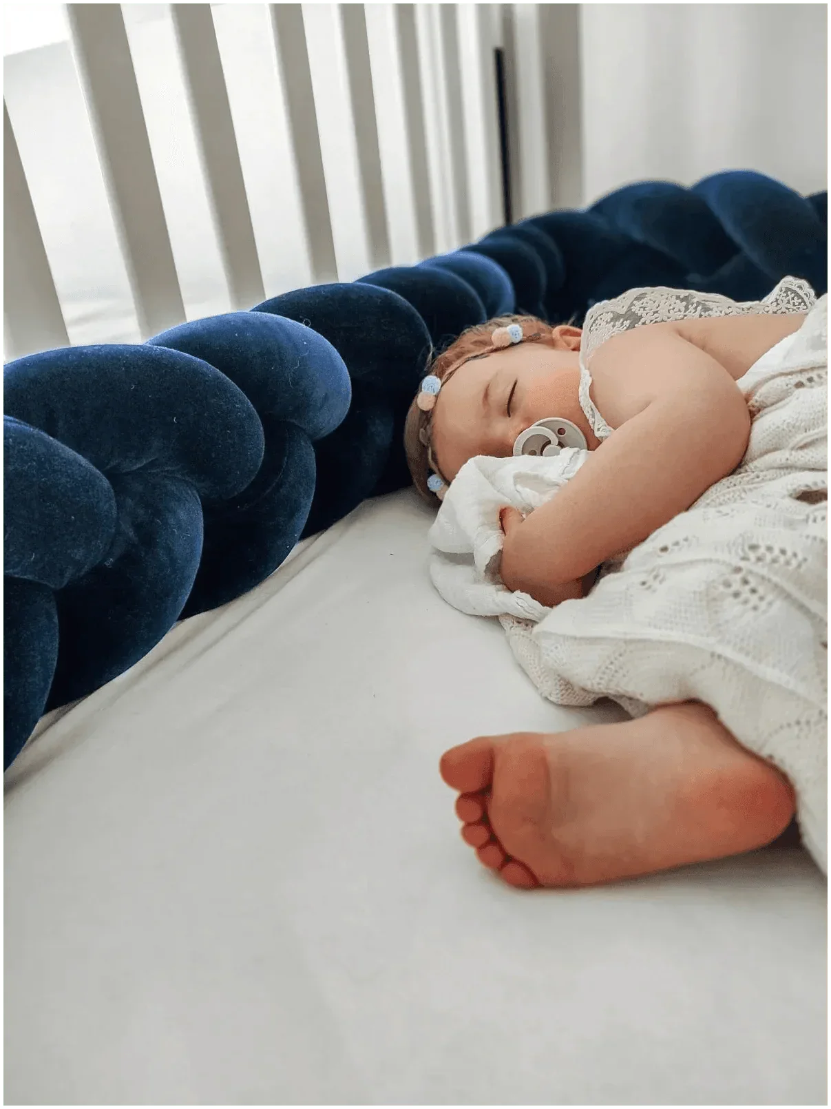Bébé dormant paisiblement avec tresse de lit bleu en velours dans un lit à barreaux.