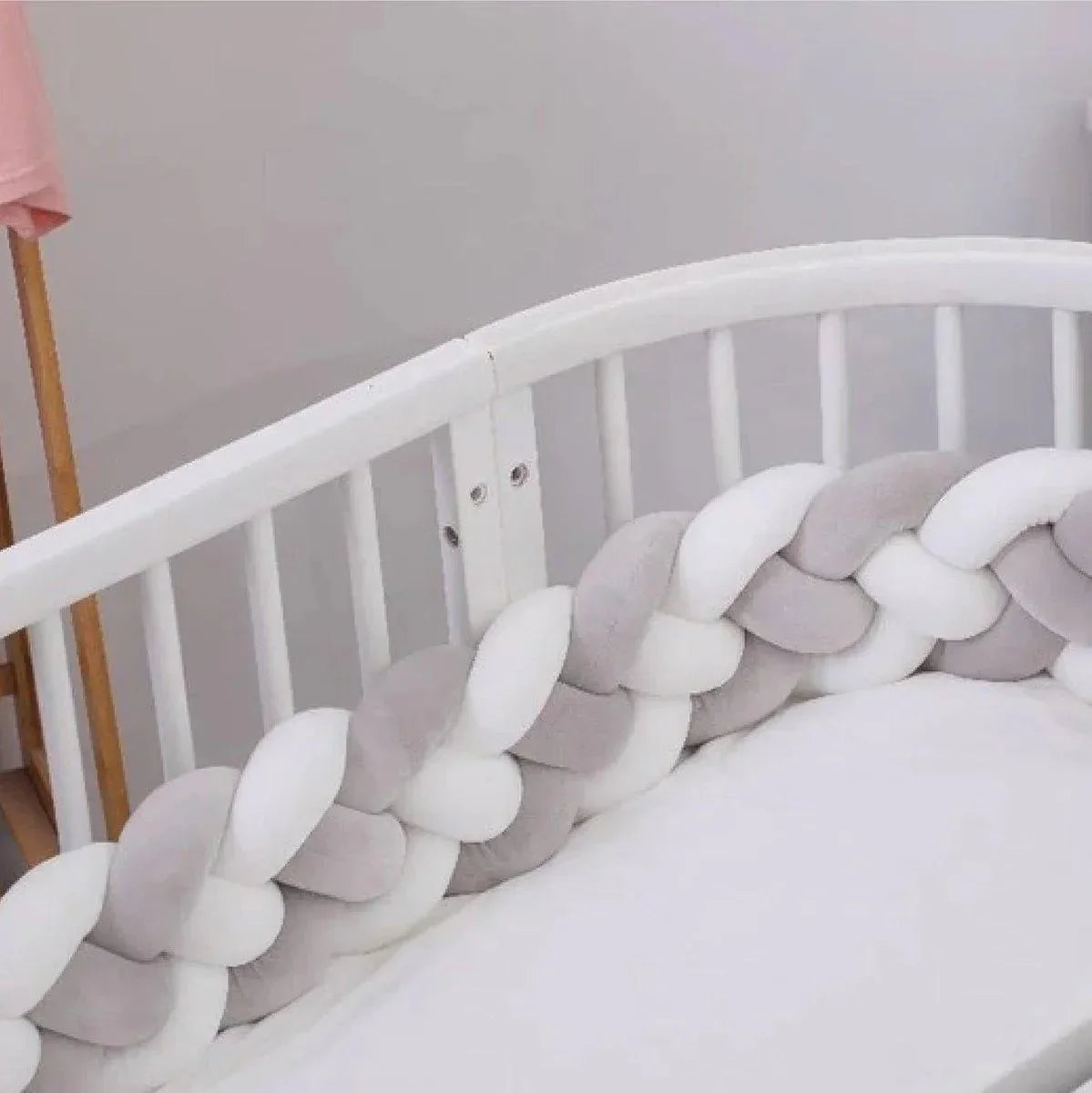 Tour de lit tressé gris et blanc en peluche, installé dans un lit bébé blanc
