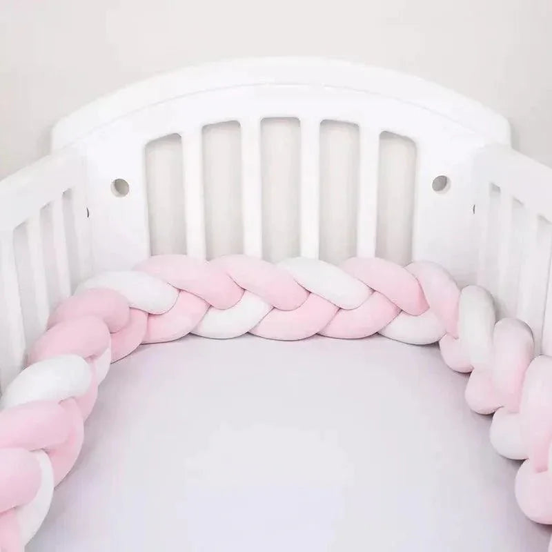 Tour de lit tressé rose et blanc, installé dans un lit bébé blanc, doux et sécurisé.