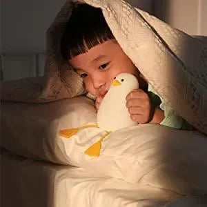 Enfant au lit câlinant une veilleuse bébé en forme de canard, ambiance rassurante.