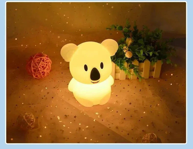 veilleuse bébé koala lumineuse, posée sur une table décorée avec plantes et étoiles dorées
