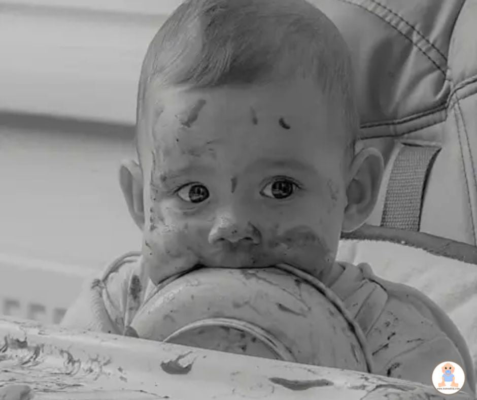 Bébé assis dans une chaise haute, visage couvert de nourriture, mordant une assiette ventouse.