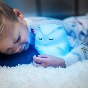 Enfant dormant avec une veilleuse bébé en forme de hibou lumineux sur un tapis moelleux.