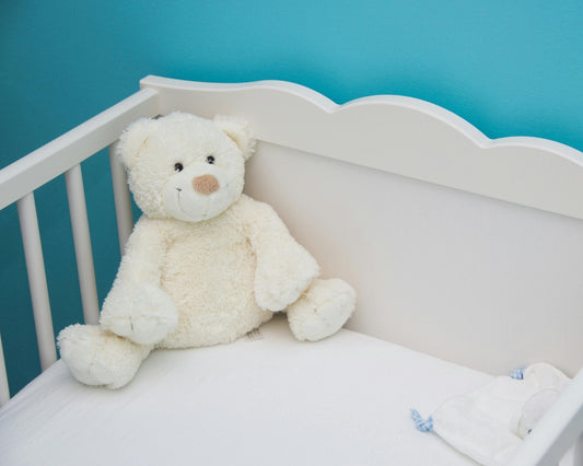 Ourson en peluche blanc rassurant dans un lit de bébé blanc, fond mur bleu apaisant