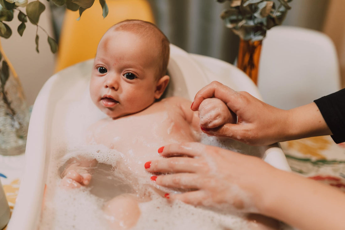 Bébé prenant un bain moussant dans une petite baignoire, main d'adulte rassurante