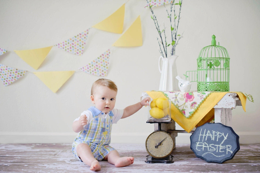 Bébé assis près d'une balance avec des citrons, décorations festives et panneau Happy Easter
