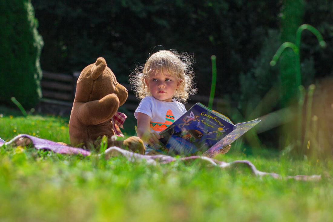 Enfant lisant un livre avec une peluche nounours sur une couverture dans le jardin