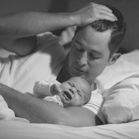 Papa berçant un bébé qui pleure dans un lit, moment de sommeil et apaisement nocturne.