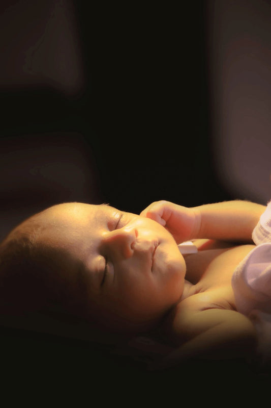 Nouveau-né endormi paisiblement dans une lumière douce, symbolisant le sommeil sécurisé du bébé.