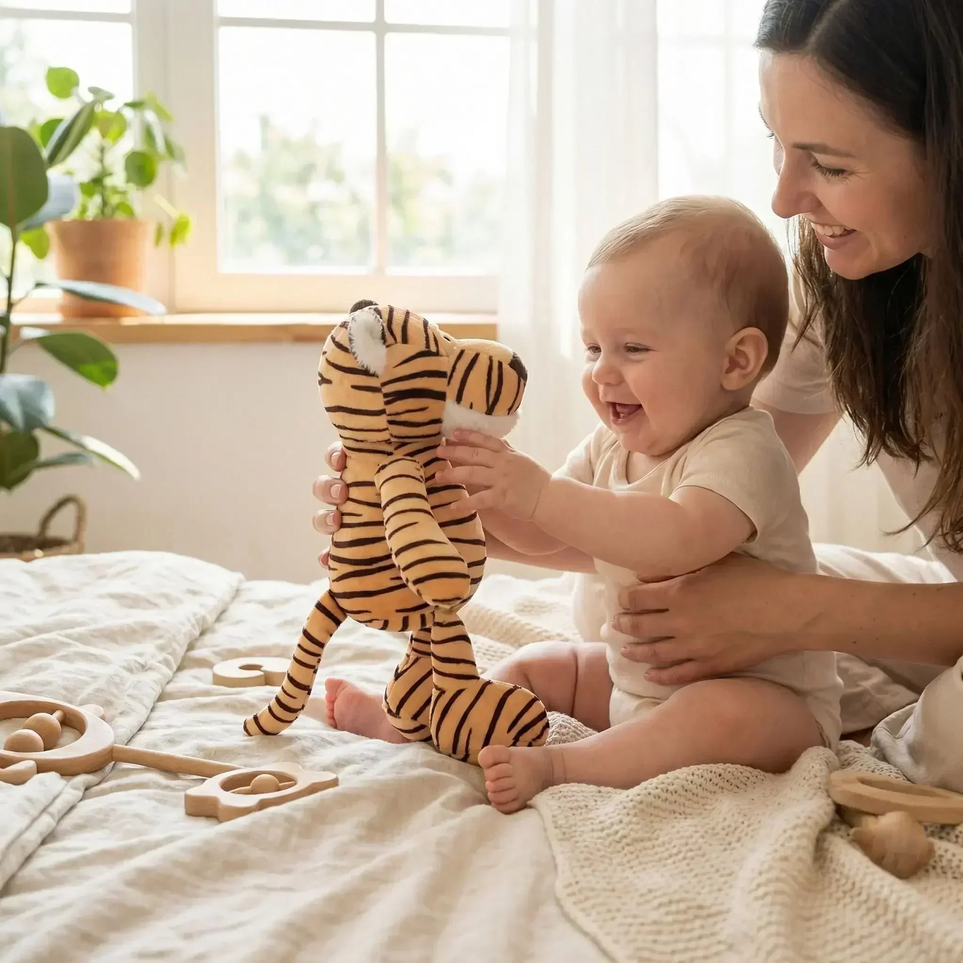 Bébé souriant joue avec un doudou tigre peluche sur un lit, accompagné de sa maman