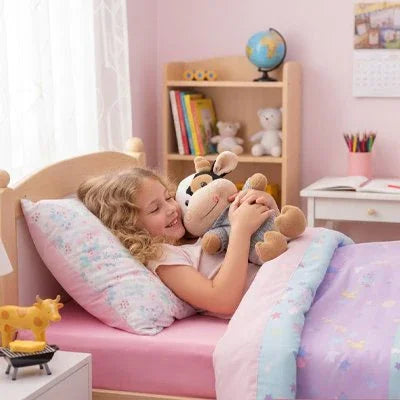 Peluche vache dans les bras d'une petite fille qui est dans son lit